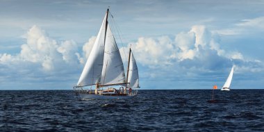Eski, pahalı, ahşap bir yelkenli (yawl) yakın çekim, açık denizde yelken. Dramatik bulut manzarası. Maine sahili, ABD