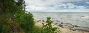 Panoramic aerial view of the rocky Baltic sea shore, pine forest. Summer. Gulf of Riga, Latvia. Dramatic sky, storm waves. Fickle weather. Vacations, travel destinations, ecotourism. Nature, seascape