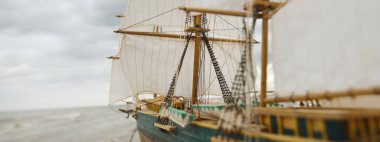 Kırpıcı uzunluğundaki geminin antik ahşap ölçekli modeli, yakın plan. Arka planda dramatik gökyüzü ve deniz kıyısı. Geleneksel zanaat, hediyelik eşya, hobi, koleksiyon, antika, modellik. Sıfır atık