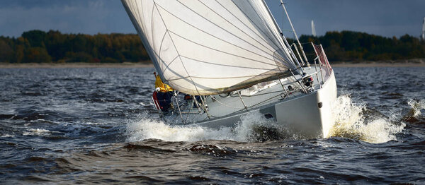 Sailing yacht regatta. Modern sailboat racing through the waves, close-up. Dramatic sky before the thunderstorm. Terrific cloudscape. North Germany, Kiel