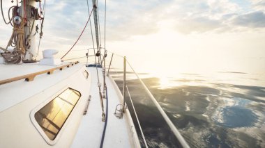 Gün batımında durgun suda yüzen beyaz bir yat. Güverteden pruvaya bir manzara, direk, yelkenler. Şaşırtıcı bulut manzarası. Sudaki yansımalar. Baltık Denizi. Yaşam tarzı, deniz yolculuğu, yelkenli yarışı, spor, eğlence