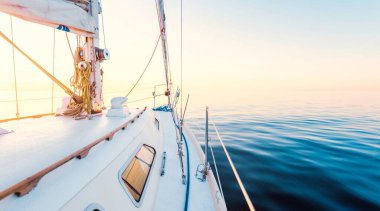 White yacht sailing in a still water at sunset. A view from the deck to the bow, mast, sails. Stunning cloudscape. Reflections on water. Baltic sea. Lifestyle, cruise, regatta, sport, recreation