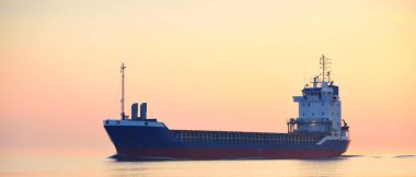 Büyük bir kargo gemisi gün batımında Baltık Denizi 'ne açılacak. Yumuşak altın güneş ışığı. Deniz manzarası kavramı. Yelkenliden panoramik görüntü. Nakliye, denizcilik, lojistik.