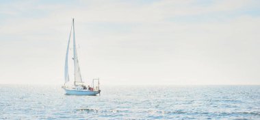 White sloop rigged yacht sailing in a Mediterranean sea on a clear sunny day, Spain. Blue sky with white clouds, reflections on water. Idyllic seascape. Sport and recreation theme