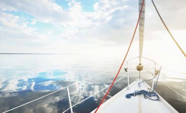 Gün batımında durgun suda yüzen beyaz bir yat. Güverteden pruvaya bir manzara, direk, yelkenler. Şaşırtıcı bulut manzarası. Sudaki yansımalar. Baltık Denizi. Yaşam tarzı, deniz yolculuğu, yelkenli yarışı, spor, eğlence