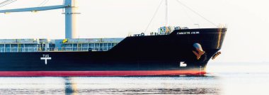 Büyük bir kargo gemisi gün batımında Baltık Denizi 'ne açılacak. Yumuşak altın güneş ışığı. Deniz manzarası kavramı. Yelkenliden panoramik görüntü. Nakliye, denizcilik, lojistik.