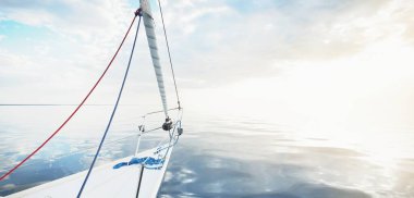 Gün batımında durgun suda yüzen beyaz bir yat. Güverteden pruvaya bir manzara, direk, yelkenler. Şaşırtıcı bulut manzarası. Sudaki yansımalar. Baltık Denizi. Yaşam tarzı, deniz yolculuğu, yelkenli yarışı, spor, eğlence