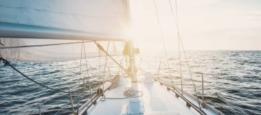 White sloop rigged yacht sailing at sunset. Clear sky after the storm. View from the deck to the bow, mast, sails. Transportation, travel, cruise, sport, recreation, leisure activity, racing, regatta
