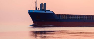 Büyük bir kargo gemisi gün batımında Baltık Denizi 'ne açılacak. Yumuşak altın güneş ışığı. Deniz manzarası kavramı. Yelkenliden panoramik görüntü. Nakliye, denizcilik, lojistik.