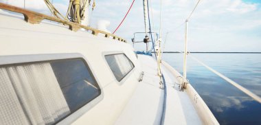 Gün batımında durgun suda yüzen beyaz bir yat. Güverteden pruvaya bir manzara, direk, yelkenler. Şaşırtıcı bulut manzarası. Sudaki yansımalar. Baltık Denizi. Yaşam tarzı, deniz yolculuğu, yelkenli yarışı, spor, eğlence