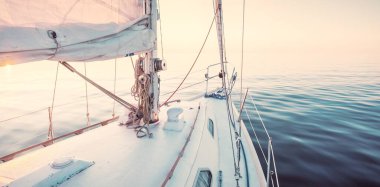 Gün batımında durgun suda yüzen beyaz bir yat. Güverteden pruvaya bir manzara, direk, yelkenler. Şaşırtıcı bulut manzarası. Sudaki yansımalar. Baltık Denizi. Yaşam tarzı, deniz yolculuğu, yelkenli yarışı, spor, eğlence