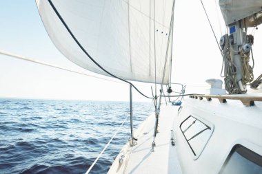 White sloop rigged yacht sailing at sunset. Clear sky after the storm. View from the deck to the bow, mast, sails. Transportation, travel, cruise, sport, recreation, leisure activity, racing, regatta
