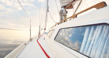 Gün batımında durgun suda yüzen beyaz bir yat. Güverteden pruvaya bir manzara, direk, yelkenler. Şaşırtıcı bulut manzarası. Sudaki yansımalar. Baltık Denizi. Yaşam tarzı, deniz yolculuğu, yelkenli yarışı, spor, eğlence