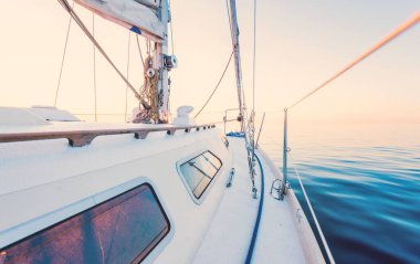 Gün batımında durgun suda yüzen beyaz bir yat. Güverteden pruvaya bir manzara, direk, yelkenler. Şaşırtıcı bulut manzarası. Sudaki yansımalar. Baltık Denizi. Yaşam tarzı, deniz yolculuğu, yelkenli yarışı, spor, eğlence