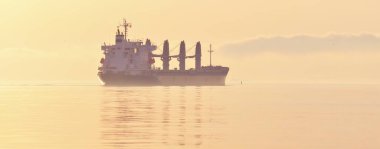 Büyük bir kargo gemisi gün batımında Baltık Denizi 'ne açılacak. Yumuşak altın güneş ışığı. Deniz manzarası kavramı. Yelkenliden panoramik görüntü. Nakliye, denizcilik, lojistik.