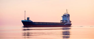 Büyük bir kargo gemisi gün batımında Baltık Denizi 'ne açılacak. Yumuşak altın güneş ışığı. Deniz manzarası kavramı. Yelkenliden panoramik görüntü. Nakliye, denizcilik, lojistik.