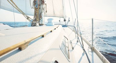 White sloop rigged yacht sailing at sunset. Clear sky after the storm. View from the deck to the bow, mast, sails. Transportation, travel, cruise, sport, recreation, leisure activity, racing, regatta