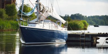 Mavi yelkenli bir yelkenli yat limanındaki bir rıhtıma demirlemiş. Tatiller, ulaşım, spor, eğlence, turizm, seyahat, liman