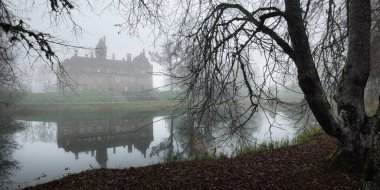 Orman parkında gölet ve kale. Jaunmoku pils, Letonya. Sis. Atmosferik sonbahar manzarası. Sessizlik, yalnızlık, melankolik kavramlar. Panoramik görünüm