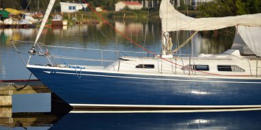 Mavi yelkenli bir yelkenli yat limanındaki bir rıhtıma demirlemiş. Tatiller, ulaşım, spor, eğlence, turizm, seyahat, liman