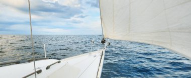 Beyaz yat gün batımında açık denizde yüzüyor. Güverteden pruva ve yelkenlere kadar yakın çekim. Fırtınadan sonra renkli bulutlarla dramatik bir gökyüzü. Dalgalar ve su sıçrıyor. Spor ve eğlence teması