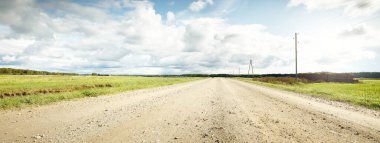 Yağmurdan sonra tarlalardan geçen boş bir köy yolu. Dramatik gökyüzü, destansı bulutlar. Hava kararsız. Transformatör direkleri yakın çekim. Letonya