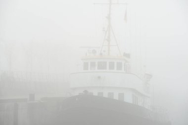 Tarihsel kargo teknesi, kalın beyaz bir sabah sisinde bir rıhtıma demirlemiş, yakın plan. Kiel, Almanya. Ulaşım, balıkçılık, yelkencilik, lojistik, endüstri, geleneksel zanaat, geçmiş, tarih. Panoramik resim