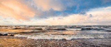 Gün batımında deniz kıyısında. Açık mavi gökyüzü, parlak pembe bulutlar, yumuşak ışık. Suyun simetri yansımaları, doğal ayna, su yüzeyi dokusu. Hava, iklim değişikliği, doğa. Idyllic deniz manzarası