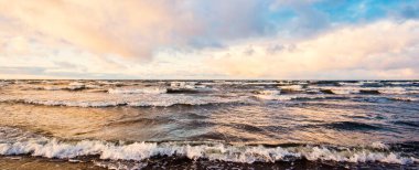 Gün batımında deniz kıyısında. Açık mavi gökyüzü, parlak pembe bulutlar, yumuşak ışık. Suyun simetri yansımaları, doğal ayna, su yüzeyi dokusu. Hava, iklim değişikliği, doğa. Idyllic deniz manzarası