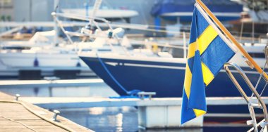 Mavi yelkenli bir yelkenli yat limanındaki bir rıhtıma demirlemiş. İsveç bayrağı yakın plan. Tatiller, ulaşım, spor, eğlence, turizm, seyahat, liman