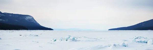 日没の凍った湖の海岸に氷の圧力尾根 背景の山のピーク 劇的な雲景 絵のように美しい冬の風景 生態系 気候変動 地球温暖化の概念 — ストック写真