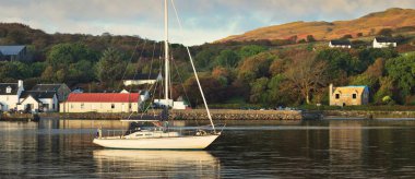 Jura adasının kıyısında demirli yelkenli bir yat. Renkli fırtınalı gün batımı gökyüzü. Geleneksel kır evleri. Dramatik bulut manzarası. Inner Hebrides, İskoçya, İngiltere