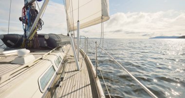 Bulutlu bir günde ahşap meşe güverteli, yelkenli, modern bir yat. Direğe ve yelkenlere bir manzara. Su, yakından sıçrıyor. Tarbert, İskoçya, İngiltere