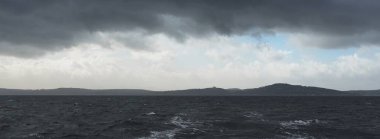 Fırtına gökyüzü. Tekne hileli modern yat, tahta meşe güvertesiyle Clyde 'ın Fırtınası' nda yelken açıyor. Arka planda Bute Adası 'nın ormanları, tepeleri ve dağları var. İskoçya, İngiltere