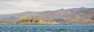 Jura adasının kıyılarının panoramik manzarası, dağları ve vadileri sudan. Bulutlu mavi gökyüzü. Paps of Jura, Inner Hebrides, İskoçya, İngiltere