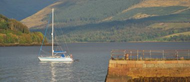 Loch Fyne yakınlarındaki sahil, orman ve tepelerin manzarası. Beyaz yelkenli yatla yakın plan. Inveraray, Inner Hebrides, Argyll ve Bute, İskoçya, İngiltere