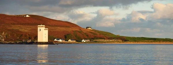 晴れた日に小さな町ポートエレンの岩場の海岸の景色 朝の日差し 古い白い灯台とカントリーハウスが近くにあります Islay Inner Hebrides スコットランド イギリス — ストック写真