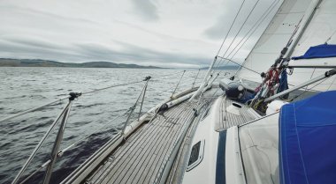 Bulutlu bir günde ahşap meşe güverteli, yelkenli, modern bir yat. Direğe ve yelkenlere bir manzara. Su, yakından sıçrıyor. Tarbert, İskoçya, İngiltere