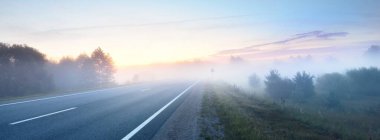 Gün doğumunda sisli bir havada boş otobanın arabasından ormana ve tarlalara doğru panoramik bir manzara. Avrupa. Ulaşım, lojistik, seyahat, yolculuk, özgürlük, sürüş. Kırsal alan