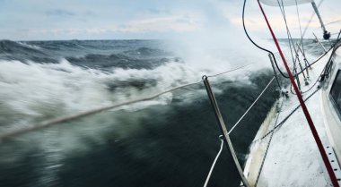 Fırtına sırasında açık denizde yelken açan beyaz bir yat. Güverteden pruvaya bak. Sert hava, dramatik gökyüzü, kara bulutlar, dalgalar, su sıçramaları. Ulaşım, seyahat, spor, eğlence aktivitesi