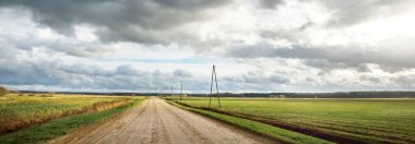 Sonbahar. Boş toprak yolun üzerindeki fırtına bulutları. Arka planda tarım alanları ve orman var. Sıcak akşam güneşi. Baltık Denizi, Garciems, Letonya