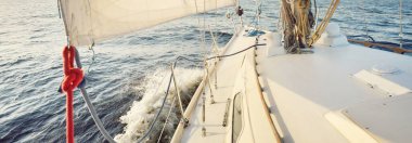 Gün batımında açık denizde yelkenli yelkenli yelkenli. Gökyüzü açık. Güverteden pruvaya bir manzara, direk, yelkenler. Ulaşım, seyahat, gezi, spor, eğlence, boş zaman aktivitesi, yarış, yelkenli yarışı