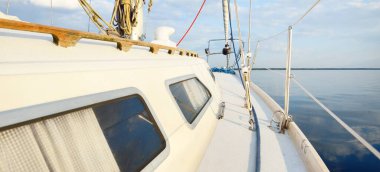 Beyaz yat gün batımında Baltık 'ta yelken açıyor. Güverteden pruvaya bak. Parlayan bulutlar, durgun suda yansımalar, doğal ayna, yumuşak altın ışık. Ulaşım, gezi, eğlence, yelkenli yarışı.