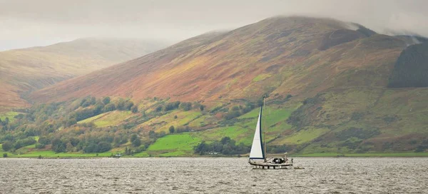 Dark storm sky. Sloop rigged yacht with a motor boat sailing on a cloudy day. Panoramic view of the rocky shores of Kyles of Bute from the water. Hills and mountains in the background. Bute island, Firth of Clyde, Scotland, UK