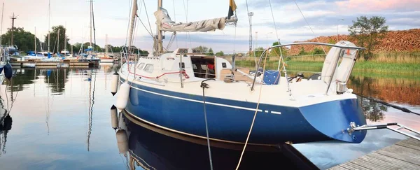 Zarif ve modern yelkenli tekneler (kiralık) açık bir günde yat limanındaki bir rıhtıma demirlediler. Ulaşım, spor ve eğlence teması. İsveç. Mavi yelkenli donanımlı yelkenli. Yakın plan.