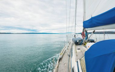 Bulutlu bir günde, Jura adasının kayalık kıyılarında seyir halindeki ahşap meşe güvertesiyle donatılmış modern bir yat. Inner Hebrides, İskoçya, İngiltere. Spor, eğlence, gezi, seyahat yerleri.