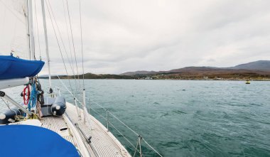 Bulutlu bir günde, Jura adasının kayalık kıyılarında seyir halindeki ahşap meşe güvertesiyle donatılmış modern bir yat. Inner Hebrides, İskoçya, İngiltere. Spor, eğlence, gezi, seyahat yerleri.