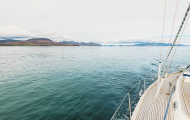 Bulutlu bir günde, Jura adasının kayalık kıyılarında seyir halindeki ahşap meşe güvertesiyle donatılmış modern bir yat. Inner Hebrides, İskoçya, İngiltere. Spor, eğlence, gezi, seyahat yerleri.