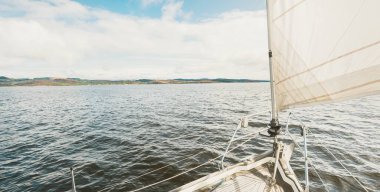 Yağmurdan sonra Tarbert 'in kayalık kıyılarında seyir halindeki ahşap meşe güvertesiyle donatılmış modern bir yat. İskoçya, İngiltere. Güverteden pruvaya, direğe ve yelkenlere yakın görüntü. Dramatik fırtına gökyüzü