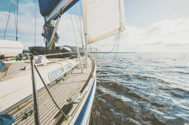 Yağmurdan sonra Tarbert 'in kayalık kıyılarında seyir halindeki ahşap meşe güvertesiyle donatılmış modern bir yat. İskoçya, İngiltere. Güverteden pruvaya, direğe ve yelkenlere yakın görüntü. Açık mavi gökyüzü